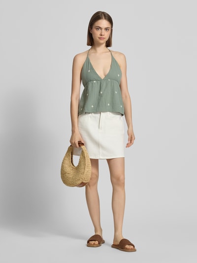 Frauenmodel trägt Crop Top aus reiner Baumwolle Modell 'THYRA RIO' von Only in Uni-Optik mit Stickereien, Regular Fit, cropped, Neckholder, V-Ausschnitt, rückenfrei, kombiniert mit weißem Rock, gedeckte Farben, weiche Textur, Ganzkörperansicht von vorne.