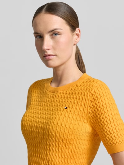 Frauenmodel trägt Damen T-Shirt Slim Fit T-Shirt aus reiner Baumwolle von Tommy Hilfiger, Optik: Unifarben, Zopfmuster, Strick, Logo-Detail, Rundhals, Kurzarm, Gerippt, Farbe Gelb, Nahaufnahme Oberkörper.