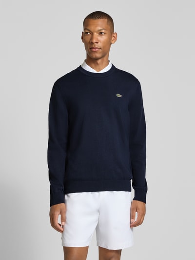 Männermodel trägt dunkelblauen Regular Fit Pullover aus Baumwoll-Mix von Lacoste, feine Strickstruktur, Ganzkörperansicht von vorne. Herren Pullover von Lacoste