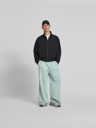 Männermodel trägt Blouson mit Stretch-Anteil von Forét in Schwarz, lockere Passform, Zweiwege-Reißverschluss, Ganzkörperansicht von vorne.