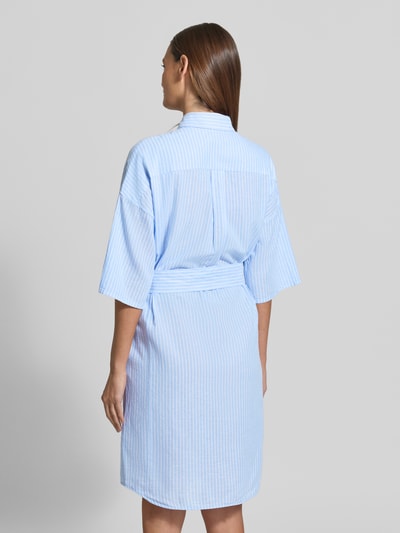 Frauenmodel trägt Knielanges Hemdblusenkleid mit Bindegürtel Modell 'DERBY' von 0039 Italy, Mieszanka lnu i bawełny, prosty krój, długość do kolan, kołnierzyk koszulowy, wiązany pasek, długość tyłu w rozmiarze S: 98 cm, szerokość w rozmiarze S: 55 cm, długość rękawów w rozmiarze S: 26 cm, niebiesko-białe paski, widoczne tekstury tkaniny, całkowity widok z tyłu.