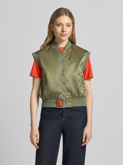 Frauenmodel trägt Weste mit Reißverschluss und Label-Detail von Original Bombers in Olivgrün, Relaxed-Fit, Stehkragen, Eingrifftaschen, Rückenlänge bei Größe S 52 cm, Schulterbreite 44 cm, Ganzkörperansicht von vorne.