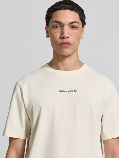Männermodel trägt Regular Fit T-Shirt aus Baumwolle von MAISON KITSUNÉ in Creme mit Rundhalsausschnitt, Label-Stitching, Nahaufnahme Oberkörper.