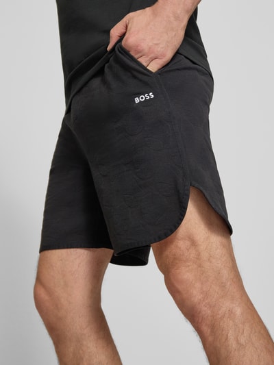 Männermodel trägt Regular Fit Shorts aus Baumwoll-Mix Modell 'JT_Member Short' von BOSS Green in Schwarz mit grafischer Struktur, Nahaufnahme Oberschenkel.
