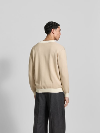 Männermodel trägt Cardigan aus reiner Baumwolle von MAISON KITSUNÉ in Beige, lockere Passform, gerippte Abschlüsse, Ganzkörperansicht Rückansicht.