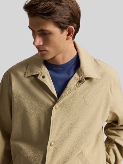 Mannenmodel draagt Regular Fit blouson uit katoenmix model 'SEERSUCKER' van Polo Ralph Lauren in effen look, gestreept patroon, platte kraag, drukknoopsluiting, gestikt logo, lange mouw met elastische mouwboord, rompzoom met tunnelkoord, zij-steekzakken, twill-stretch materiaalverwerking. Nahaufnahme bovenlichaam.