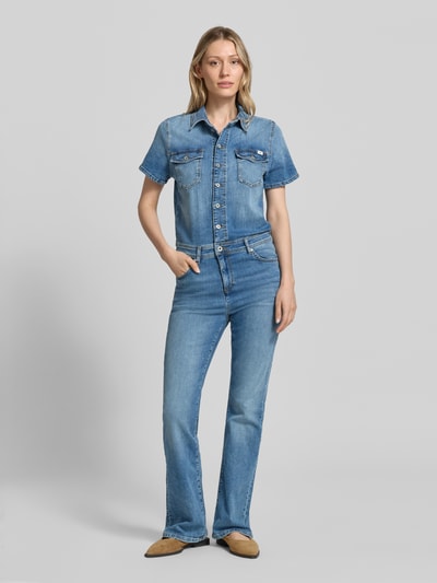 Frauenmodel trägt Flared Denim-Jumpsuit Modell 'KIMMY' von Mustang aus Baumwoll-Elasthan-Mix mit Knopfleiste, Brusttaschen, Label-Detail, Denim in mittlerem Blau, Umlegekragen, Ganzkörperansicht von vorne, Rückenlänge 53 cm, Brustweite 46 cm, Ärmellänge 20 cm, Gesamtlänge 165 cm, Innenbeinlänge 83 cm bei Größe S.