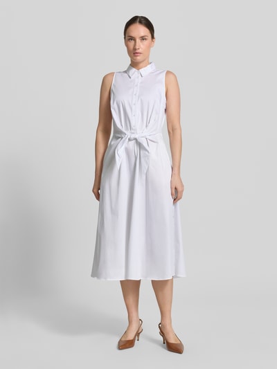Frauenmodel trägt Hemdblusenkleid aus Satin in Midilänge von Comma in Weiß, taillierte Passform, durchgehende Knopfleiste, abnehmbares Taillenband, Ärmelloses-Design, Baumwoll-Mix, glatte Textur, Ganzkörperansicht von vorne.