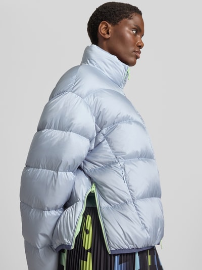 Frauenmodel trägt Regular Fit Jacke in Stepp-Optik mit Stehkragen von Marc Cain in hellem Blau, glänzende Oberfläche, Steppnähte, Nahaufnahme Oberkörper, Kontext: Zweiwege-Reißverschluss, elastische Abschlüsse, Rückenlänge 50 cm, Schulterbreite 39 cm, Brustweite 57 cm, Ärmellänge 52 cm.