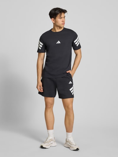 Männermodel trägt Regular Fit T-Shirt aus reiner Baumwolle von adidas Sportswear, unifarben mit Logo-Print und Kontraststreifen, Ganzkörperansicht von vorne.