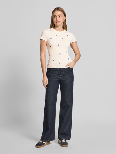 Kobiece modelka nosi T-Shirt in Ripp-Optik mit Stitchings von Jake*s Casual, mieszanka bawełny (bio) i elastanu, krój slim fit, efekt prążkowania, hafty, długość tyłu w rozmiarze S 55 cm, ciemnoniebieskie spodnie, kremowy t-shirt w niebieskie hafty, całkowity widok z przodu.