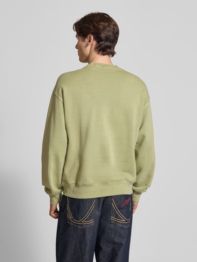 Männermodel trägt Sweatshirt mit Label-Detail Modell 'Nelson' von Carhartt Work In Progress aus Reine Baumwolle in Grün, Relaxed-Fit, Rückenlänge 68 cm, Ärmellänge 63 cm, Ganzkörperansicht Rückansicht.