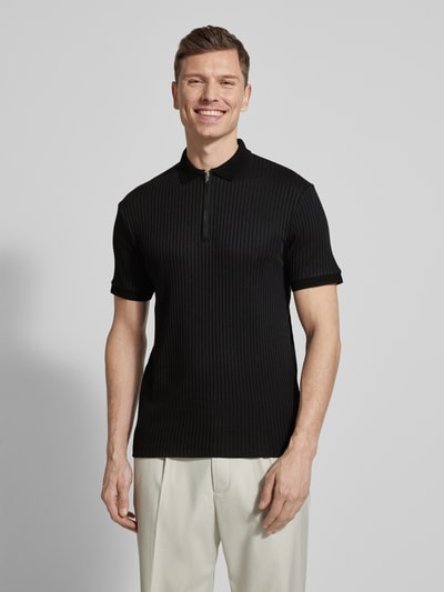 Mężczyzna nosi Regular Fit Poloshirt mit Bio-Baumwoll-Anteil Modell 'FAVE' od SELECTED HOMME, czarny, krótki rękaw, krój regular fit, zamek, kołnierzyk polo, ściągacze, materiał prążkowany, widok całej sylwetki z przodu.