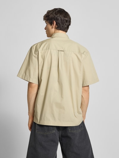 Männermodel trägt Relaxed Fit Freizeithemd mit Kentkragen und Label-Detail von Carhartt Work In Progress in Beige, Rückenansicht, Material-Mix mit Baumwoll-Anteil, kurze Ärmel, Brusttaschen sind nicht sichtbar, Struktur glatter Stoff. Ganzkörperansicht Rückansicht.