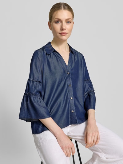 Frauenmodel trägt Regular Fit Jeansbluse aus Lyocell von s.Oliver BLACK LABEL in Denim-Optik mit Hemdblusenkragen, Frill Detail, V-Ausschnitt, einreihiger Knopfleiste und Trompetenärmel, Material Lyocell, Nahaufnahme Oberkörper.