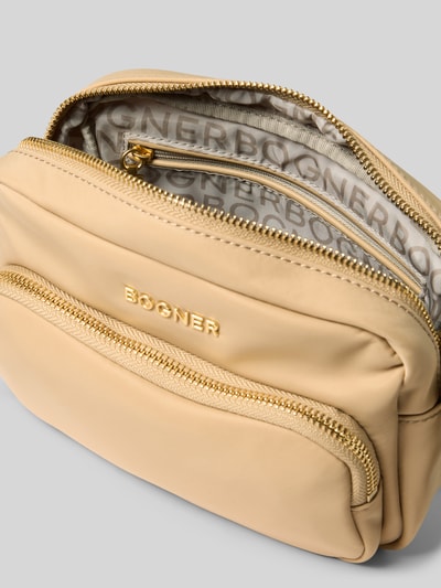 Produktfoto, beigefarbene Umhängetasche mit Label-Detail Modell 'klosters neve lidia' von BOGNER, glatte Oberfläche, goldfarbener Reißverschluss, Innenfutter mit Markenprint, Breite 20 cm, Länge 14 cm, Tiefe 9 cm, Schulterriemen 110 cm.