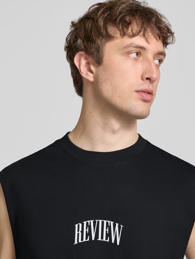 Männermodel trägt Muskelshirt mit Logo und Rundhalsausschnitt von REVIEW, schwarze Baumwolle, Regular Fit, Nahaufnahme Oberkörper.