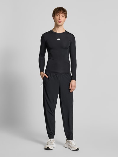 Mannenmodel draagt Shirt met lange mouwen met labelprint van adidas Training, materiaalmix met stretch, slim fit, ruglengte maat M 65 cm. Volledige lichaamsaanzicht van voren.