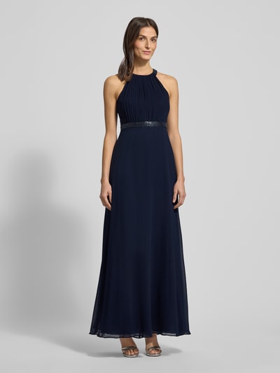 Frauenmodel trägt Abendkleid mit Ziersteinbesatz und Raffungen von V.M. by Vera Mont aus dunkelblauem Chiffon, Unifarbenes Design, Maxi-Länge, taillierter Schnitt, Neckholder, Hakenverschluss, mit blickdichtem Unterrock, Ganzkörperansicht von vorne.