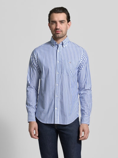 Männermodel trägt Slim Fit Freizeithemd mit Brusttasche von Gant, blau-weiß gestreift, reine Baumwolle, Logo-Stitching, Ganzkörperansicht von vorne.