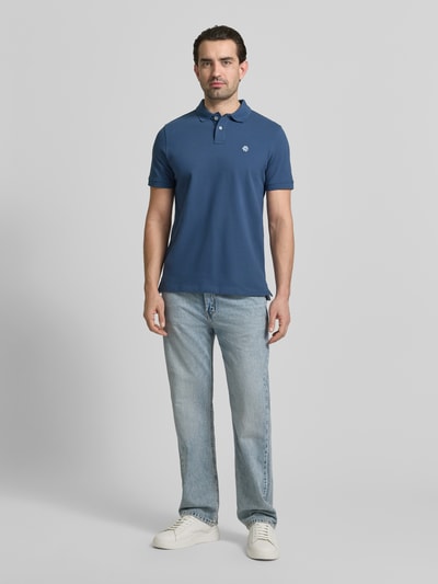 Männermodel trägt Slim Fit Poloshirt mit Logo-Stitching von MCNEAL in Blau, reine Baumwolle, Polokragen, Ganzkörperansicht von vorne.