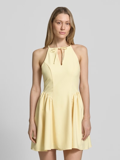 Frauenmodel trägt Cocktailkleid mit Schlüsselloch-Ausschnitt von Little Mistress aus Material-Mix mit Rayon-Anteil, A-Linie, Minikleid, Schnürung, Rückseitiger Reißverschluss, in hellem Gelbton, glatte Textur, Ganzkörperansicht von vorne.