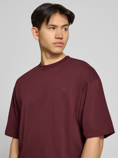 Männermodel trägt Oversized T-Shirt mit Logo und Rundhalsausschnitt von REVIEW in Dunkelrot aus Reine Baumwolle, Nahaufnahme Oberkörper.