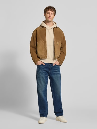 Männermodel trägt blaue Tapered Fit Jeans aus Baumwoll-Mix von Tommy Jeans, kombiniert mit hellen Sneakern, Ganzkörperansicht von vorne, Herren Tapered Fit Jeans von Tommy Jeans.