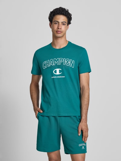 Männermodel trägt T-Shirt mit Label-Print und Rundhalsausschnitt von CHAMPION, Herren T-Shirt, Reine Baumwolle, Regular-Fit, Ganzkörperansicht von vorne.