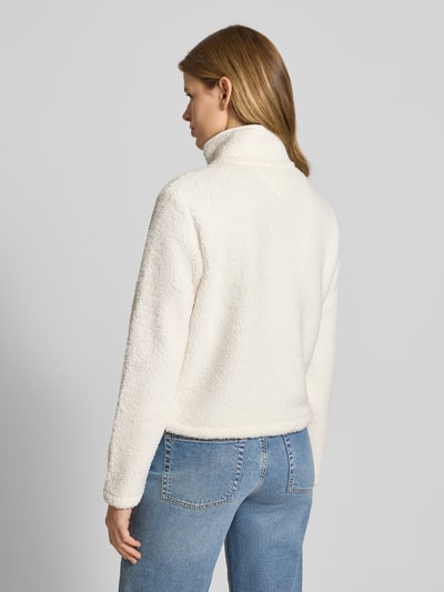 Modelka nosi Regular Fit Teddy-Jacke mit verdecktem Reißverschluss od Tommy Jeans, efekt: jednolity kolor, stójka, imitacja futerka, długi rękaw, kieszenie zapinane na zamek błyskawiczny, wyhaftowane logo, wykończenie materiału: futerko, widok całej sylwetki z tyłu.