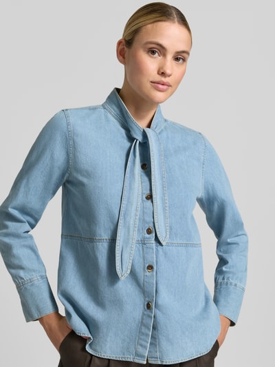 Modelka nosi Regular Fit Hemdbluse aus reiner Baumwolle in Denim-Optik von Emily Van den Bergh, tkanina stylizowana na denim, stójka, bluzka z długim rękawem, długość tyłu w rozmiarze 36: 61 cm, długość rękawów w rozmiarze 36: 58 cm, jasnoniebieska, gładka faktura, widoczne przeszycia, całkowite ujęcie przodu.