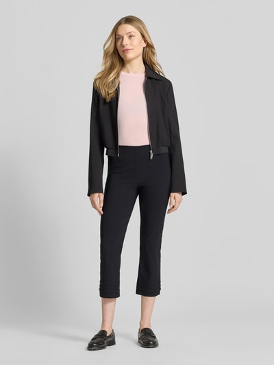 Kobieta nosi spodnie capri z mieszanki wiskozy model 'Ina' od STEHMANN, krój slim fit, drapowania, długość 7/8, czarny, szerokość w rozmiarze 36: 38 cm, długość wewnętrzna nogawki: 59 cm, z dodatkiem streczu, widok całej sylwetki z przodu.