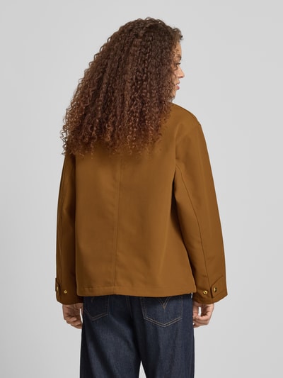 Männermodel trägt Jacke mit Stehkragen und Zweiwege-Reißverschluss Modell 'Clark' von Carhartt Work In Progress, krój relaxed fit, detal z logo, kolor brązowy, szerokość ramion w rozmiarze S 50 cm, szerokość klatki piersiowej w rozmiarze S 54 cm, długość tyłu w rozmiarze S 66 cm, długość rękawów w rozmiarze S 58 cm, widok całej sylwetki z tyłu