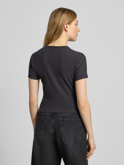 Frauenmodel trägt Cropped T-Shirt mit geripptem Rundhalsausschnitt von Scotch & Soda aus Baumwoll-Elasthan-Mix, Slim Fit, Rückenlänge 46 cm, dunkle Farbe, strukturierte Oberfläche, Ganzkörperansicht Rückansicht.