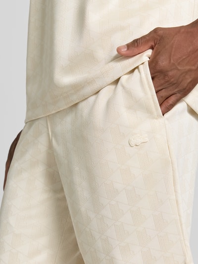 Männermodel trägt Regular Fit Sweatshorts mit Monogramm-Logo-Print von Lacoste in Beige mit feiner Textur, Nahaufnahme Oberkörper, Herren Sweatshorts von Lacoste.