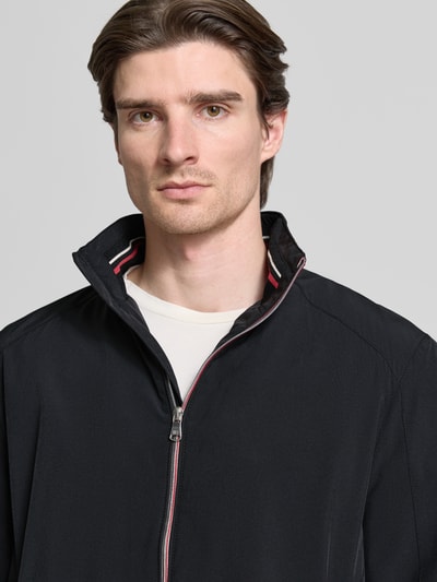 Männermodel trägt Jacke mit Stehkragen von Christian Berg Men in Schwarz mit Reißverschlusstaschen und gerippten Abschlüssen, Nahaufnahme Oberkörper. Material-Mix mit Stretch, lockerer Schnitt, Stehkragen, Maße Größe M.