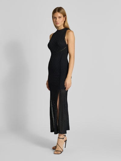 Modelka prezentuje długą sukienkę Maxikleid mit Spitze und Gehschlitz Modell 'NEW LIZA' od Guess, czarny kolor, koronka, okrągły dekolt, dopasowany krój, rozporek z boku, tylny detal z logo, halka pod sukienkę, mieszanka materiałów z dodatkiem streczu, półprzezroczysty materiał, widoczna tekstura koronki, całkowity widok z przodu