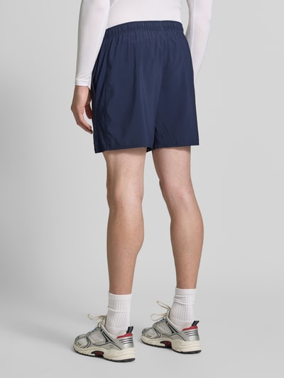 Mężczyzna nosi szorty Regular Fit Shorts mit integriertem Slip Modell 'ICON' od ASICS TIGER, niebieskie, elastyczny pas, nadruk z logo, szerokość w rozmiarze M: 37 cm, długość wewnętrzna nogawki: 18 cm, krój regular fit, widok całej sylwetki z tyłu