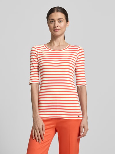 Frauenmodel trägt T-Shirt mit Halbarm von Marc Cain im orange-weiß gestreiften Baumwoll-Elasthan-Mix, körpernah, Rundhalsausschnitt, Ganzkörperansicht von vorne.