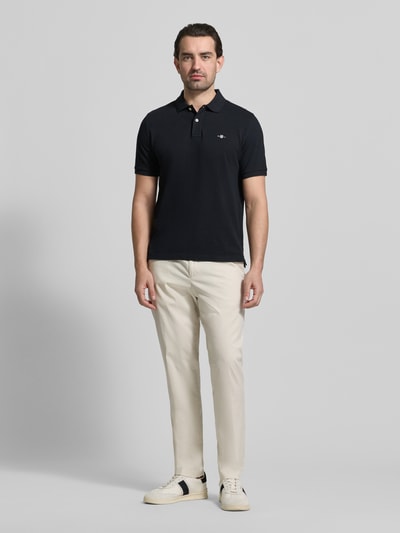 Męski model nosi Slim Fit Poloshirt mit Logo-Stitching od Gant, czysta bawełna, krój slim fit, granatowy, widok całej sylwetki z przodu.