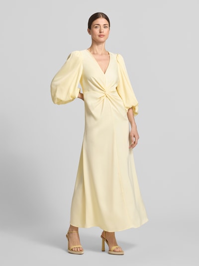 Frauenmodel trägt Maxikleid mit Ballonärmeln Modell 'THEA' von YAS, Material-Mix mit Stretch-Anteil, Taillierter Schnitt, V-Ausschnitt, Knoten-Detail, Rückenlänge 35 cm, Brustweite 32 cm, Ärmellänge 49 cm, sanftes Gelb, glatte Textur, Ganzkörperansicht von vorne.