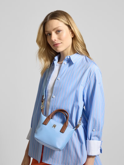Frauenmodel trägt Henkeltasche mit Logo-Applikation aus Metall Modell 'POPETTE MICRO' von Tommy Hilfiger, Optik: Unifarben, Blautöne mit braunen Leder-Applikationen, Reißverschluss, Hauptfach, Reißverschlussfach innen, Tragehenkel, abnehmbarer Schulterriemen, Nahaufnahme Oberkörper.