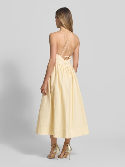Frauenmodel trägt Midikleid mit Eingrifftaschen Modell 'COVER' von SUNCOO PARIS aus Baumwoll-Mix in A-Linie, Spaghettiträger, rückseitige Schnürung, Farbe hellgelb, strukturierte Oberfläche, Ganzkörperansicht Rückansicht.
