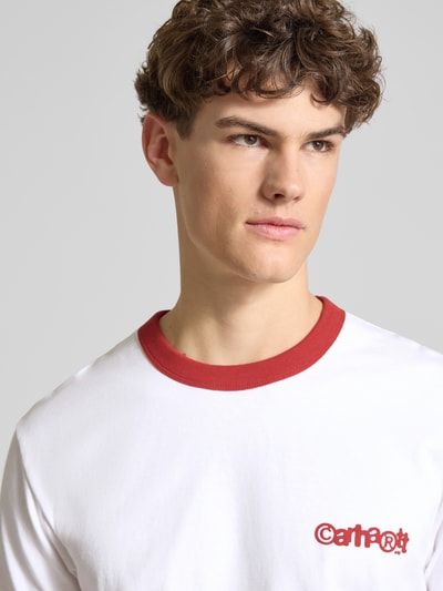 Männermodel trägt T-Shirt im Retro-Look mit Label-Print von Carhartt Work In Progress, weiß mit rotem Rundhalsausschnitt, Nahaufnahme Oberkörper.