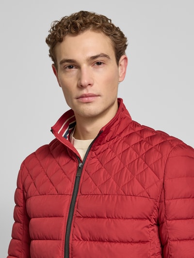 Męski model ma na sobie Slim Fit Steppjacke mit gefüttertem Kragen von Christian Berg Men, czerwony pikowany materiał, kieszenie zapinane na zamek błyskawiczny, ocieplany kołnierz, elastyczne zakończenia rękawów, zamek błyskawiczny, długość tyłu w rozmiarze M: 68 cm, szerokość ramion w rozmiarze M: 47 cm, szerokość w rozmiarze M: 52 cm, długość rękawów w rozmiarze M: 68 cm, Nahaufnahme górnej części ciała.