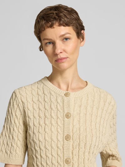 Kobiece model prezentuje kardigan z mieszanki bawełny i lnu model 'Diva' od My Essential Wardrobe, krój regular fit, ścieg warkoczowy, okrągły dekolt, listwa guzikowa, rękaw o dł. 1/2, kolor beżowy, wyraźna tekstura, damski kardigan, detaliczny widok górnej części ciała