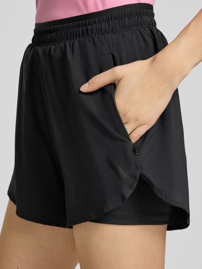 Frauenmodel trägt schwarze Regular Fit Shorts mit Reißverschlusstaschen von adidas Sportswear, elastischer Bund, Nahaufnahme Oberschenkel.