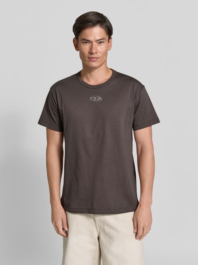 Männermodel trägt Regular Fit T-Shirt aus reiner Baumwolle von Diesel in Dunkelbraun mit Logo-Detail und Rundhalsausschnitt, Ganzkörperansicht von vorne. Rückenlänge bei Größe M: 72 cm, kurzärmeliges Design.