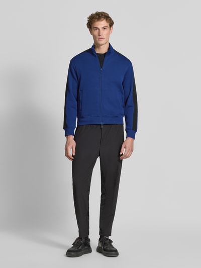 Männermodel trägt Regular Fit Sweatjacke aus Baumwoll-Mix Modell 'Felpa' von Armani Exchange in Blau mit schwarzen Details, Ganzkörperansicht von vorne. Elastischer Baumwoll-Mix, Stehkragen, Zweiwege-Reißverschluss, Eingrifftaschen, elastische Abschlüsse, Rückenlänge 64 cm, Ärmellänge 62 cm.