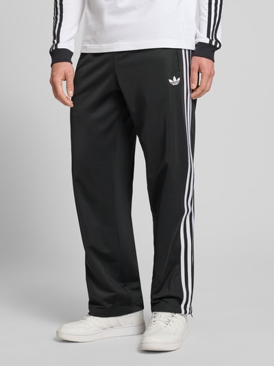 Männermodel trägt Sweatpants mit elastischem Bund von adidas Originals in Schwarz mit weißen Streifen, lockerer Schnitt, Nahaufnahme Unterkörper.